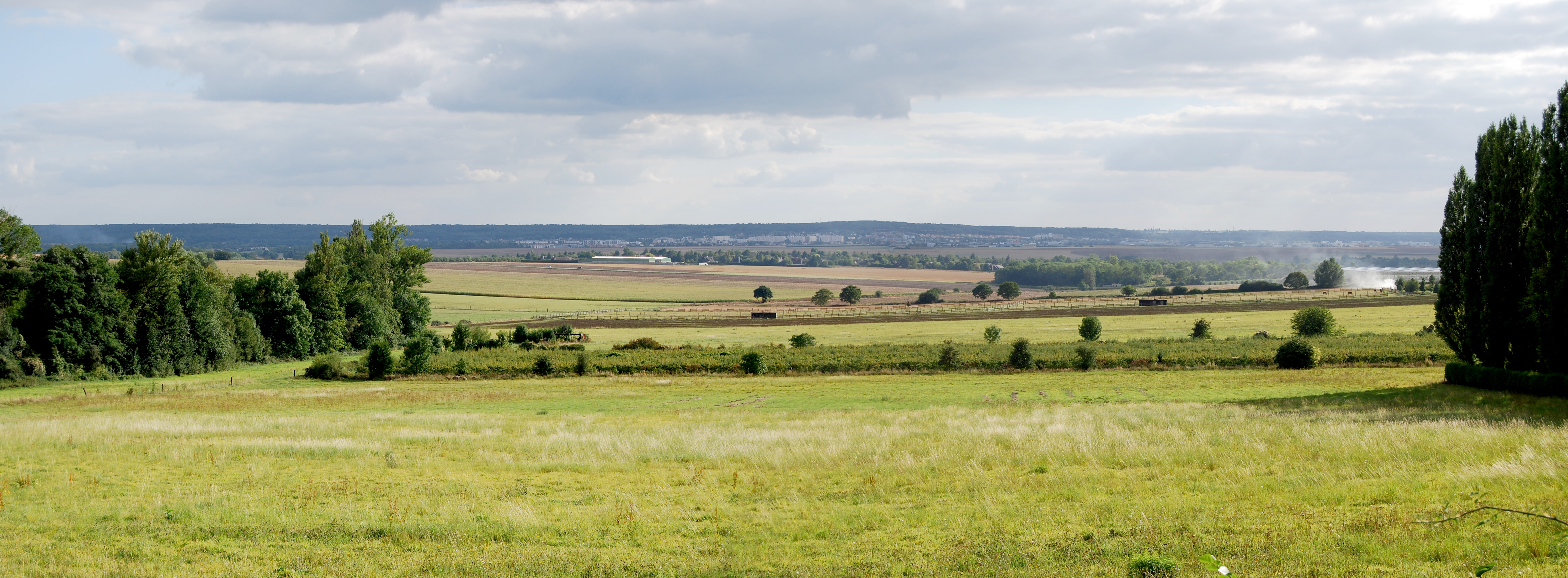 La plaine de Versailles dans toute sa largeur, avec à l’horizon le rebord boisé du plateau de l’Yveline et du Hurepoix, au pied duquel s’étendent Villepreux et les Clayes-sous-Bois. Vue depuis la lisière de la forêt de Marly à Feucherolles